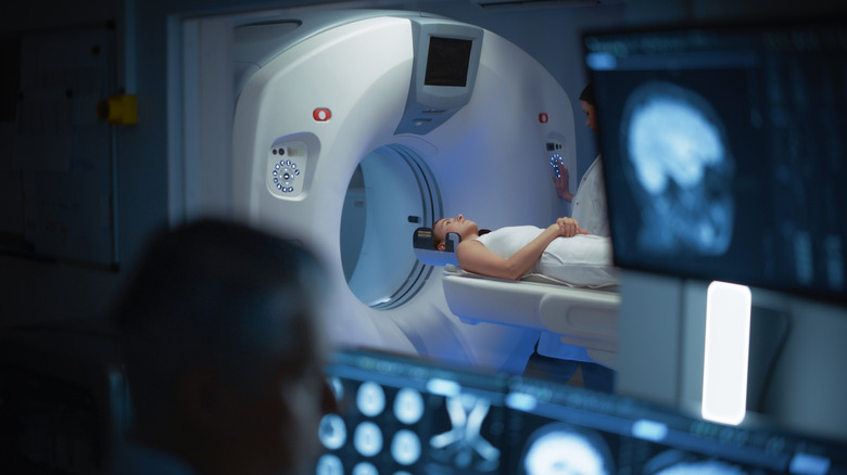 A woman enters the tube of an MRI machine, as a technician