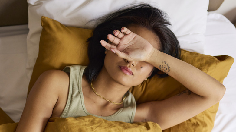 Woman with arm over eyes laying in bed