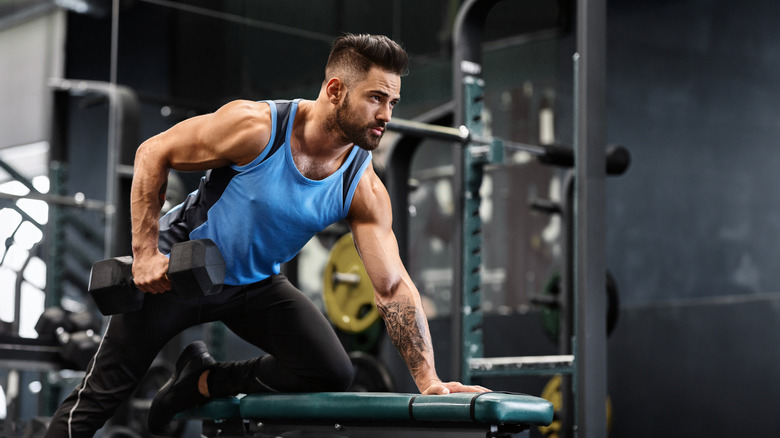 man in gym doing one-arm dumbbell rows on a weight bench
