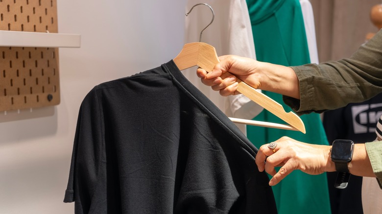 Hands taking black shirt off a hanger