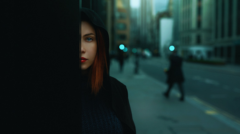 Woman wearing black and hiding behind a wall