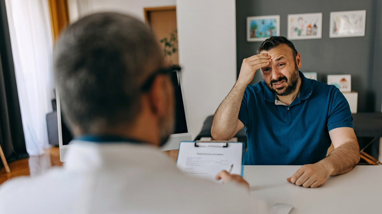 Man with hand on head describing symptoms to a doctor
