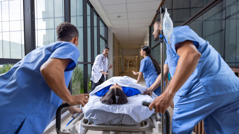 A woman on a gurney is rushed by hospital staff down a hallway