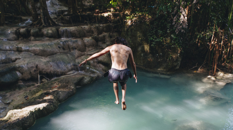 White man jumping into jungle pool, vines and rocks surrounding