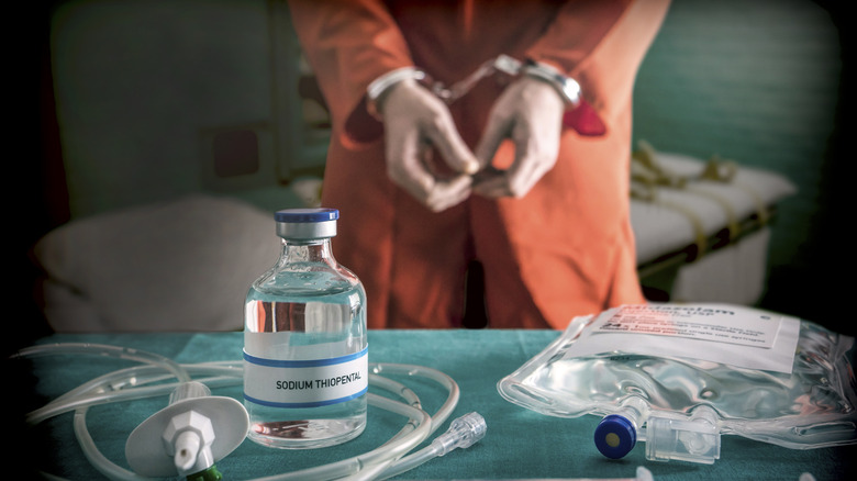 Handcuffed person in prison jumper looks at table with vial of sodium thiopental