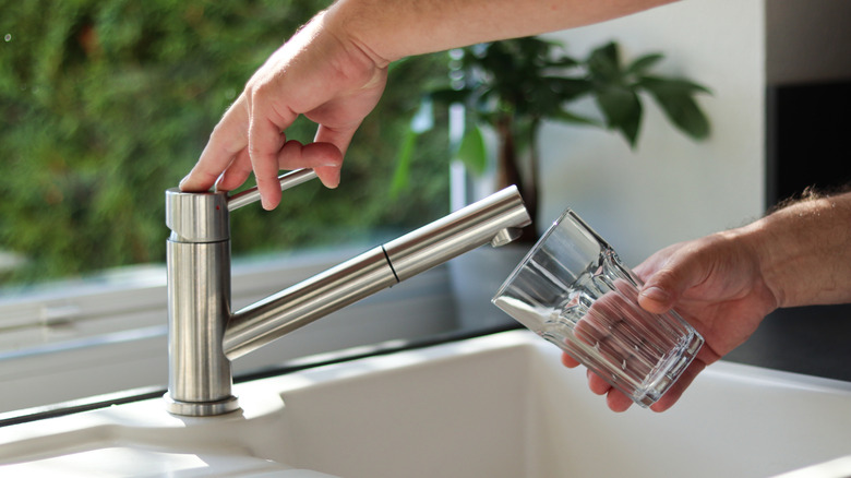 Close up of male hands pouring tap water into a glass in the kitchen