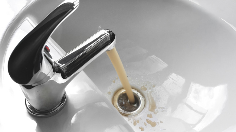 Dirty water flows from a faucet in a white bathroom sink