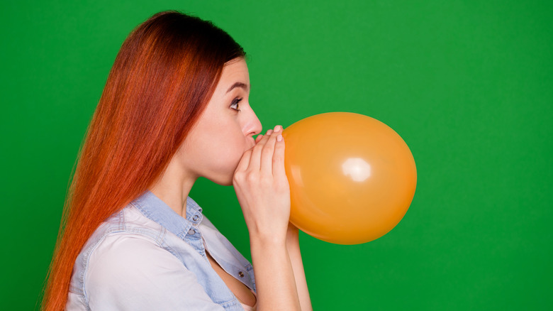 redheaded woman inhaling from orange balloon
