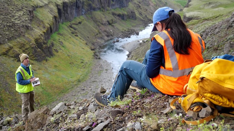 NASA scientists in river valley of Iceland, green grassy hills and scientists in neon vests