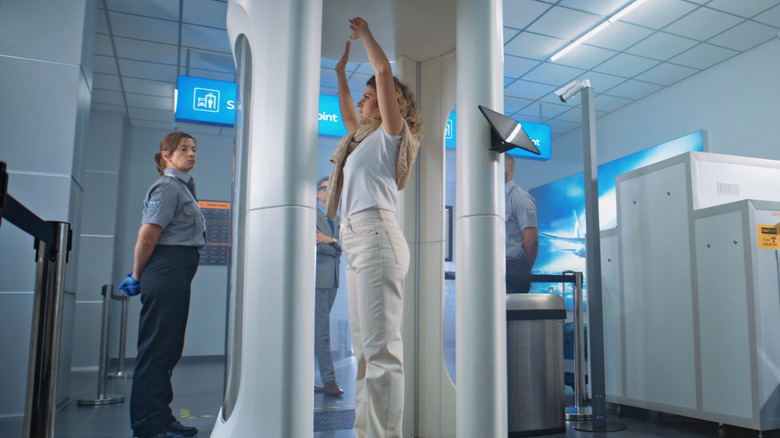 A woman holds her hands above her head as she stands inside a full body scanner in an airport