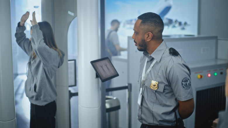An airport security officer watches a woman standing inside a body scanner