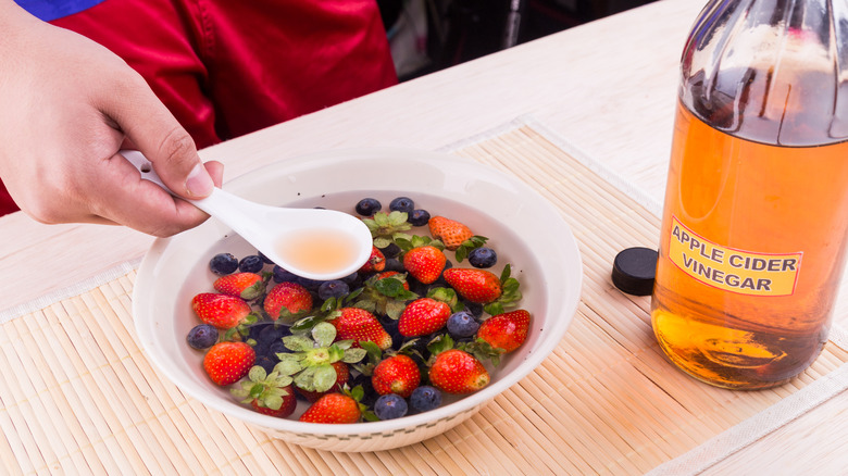 Person adding vinegar to bowl of berries in water