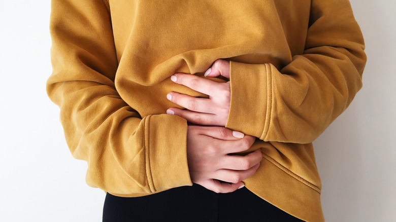 A person in a large, yellow sweatshirt holding their belly.