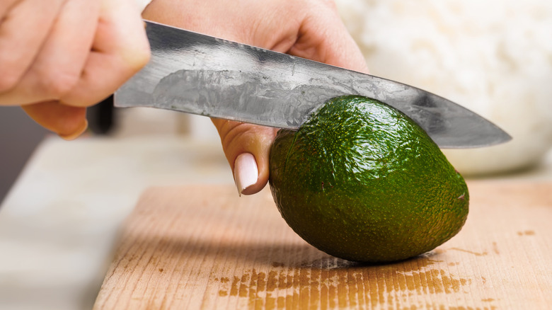 Close up of person cutting avocado with metal knife