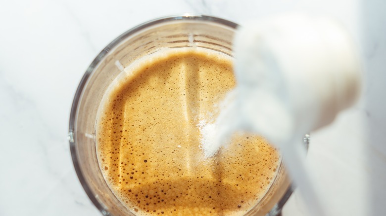 Powdered creamer poured into foamy coffee in a glass