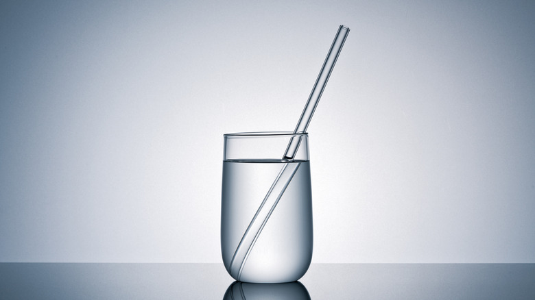 Clear glass of water with a straw that looks bent on a soft gray background