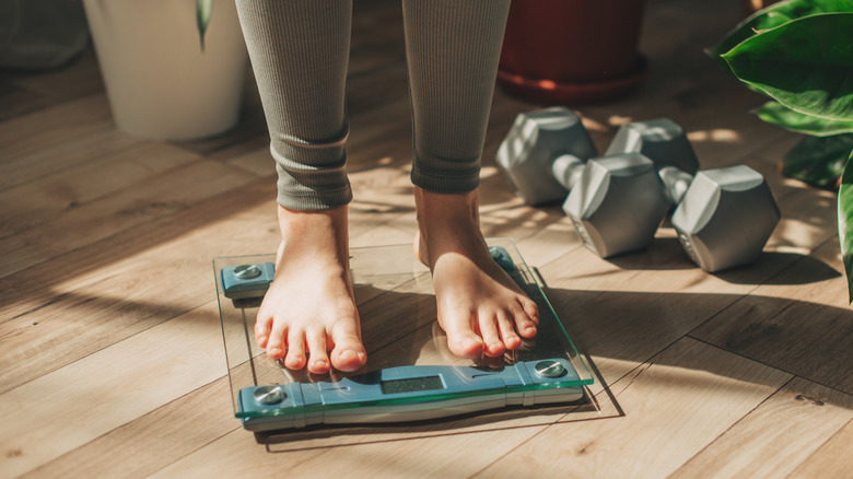 A woman's feet are seen on a scale alongside some small weights and a plant
