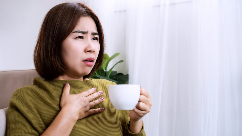 Woman experiencing unwanted effects after drinking cup of coffee