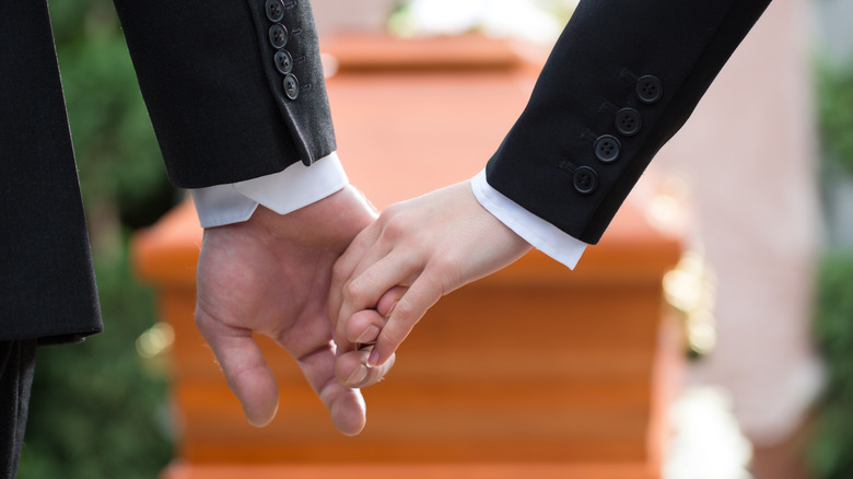 Man and woman hold hands standing in front of a casket