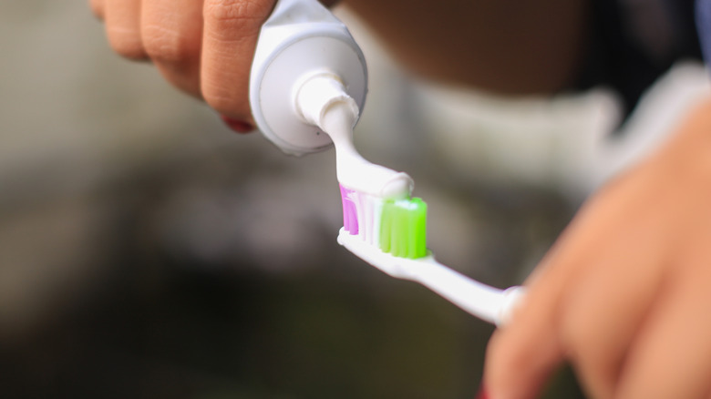 Person putting toothpaste on a toothbrush with pink, white, and green bristles