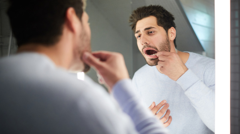 Man looking at teeth in a bathroom mirror