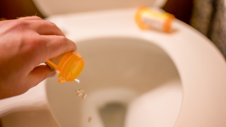 Hand pouring contents of medicine bottle down a toilet