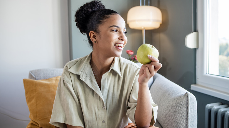 Woman holding green apple while sitting on couch