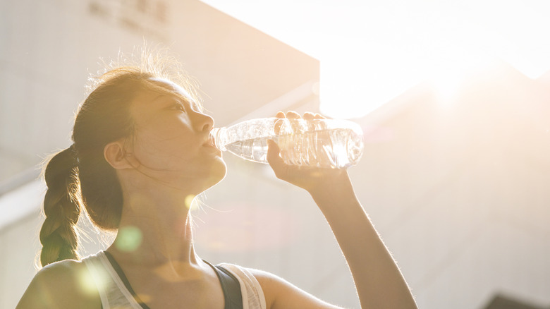 A woman with a pony tail drinks from an unlabeled plastic water bottle