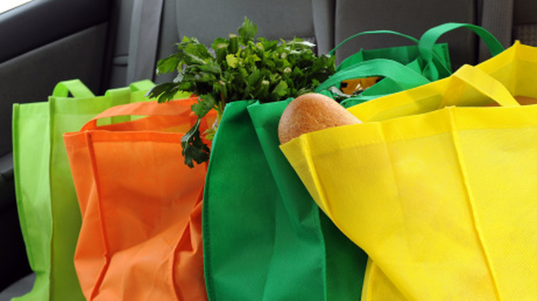 Green, orange, and yellow reusable grocery bags holding groceries