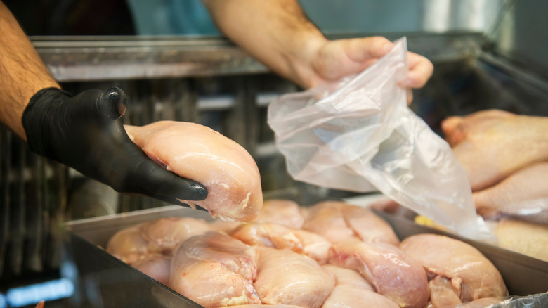 Hands of a butcher putting chicken into a clear plastic bag