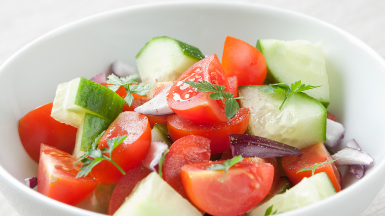 Salad of tomatoes, cucumbers, red onion, and parsley in a white bowl