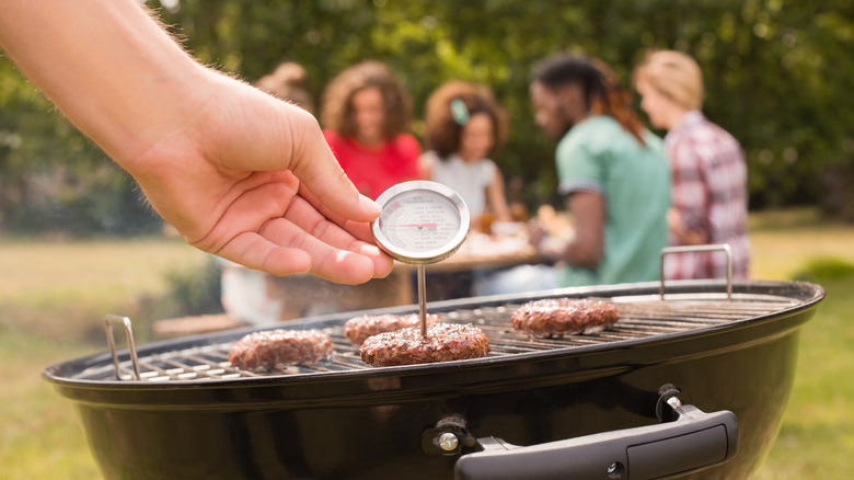 Person checking burgers on grill with a meat thermometer