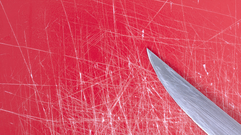 Heavily scratched surface of a red plastic cutting board