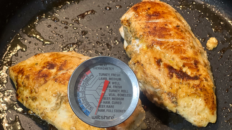 Chicken cooking in a pan with a meat thermometer to check temperature