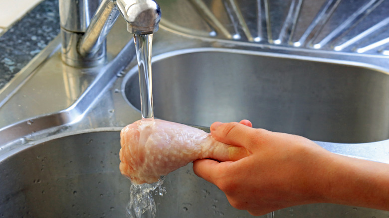 Person washing chicken leg under faucet