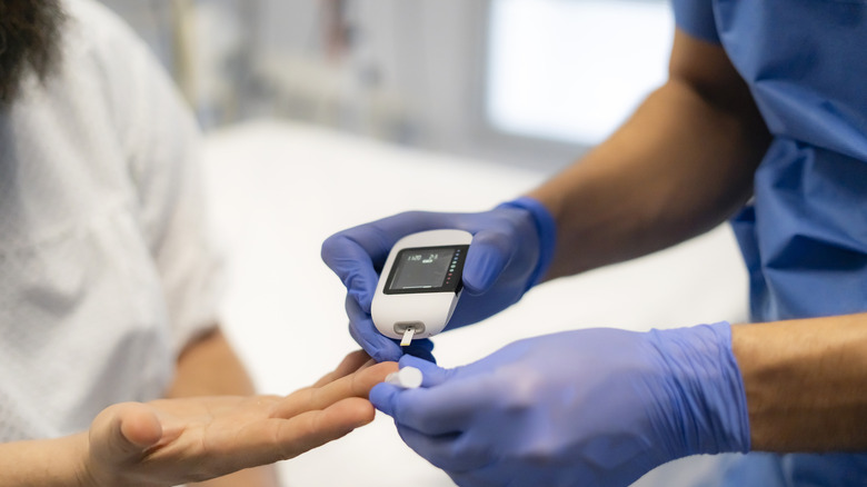 A doctor wearing blue gloves measures a woman's blood sugar levels with a glucometer