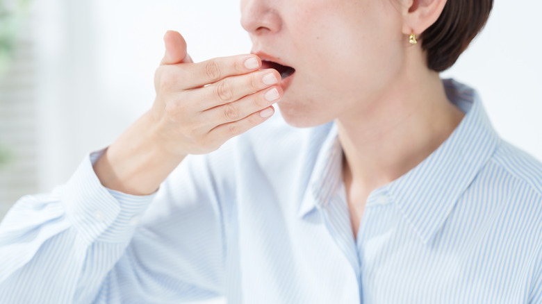 A woman in a blue and white striped shirt holding her hand in front of her mouth to check her breath