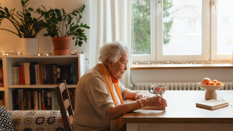 An elderly person reading a book at a table.