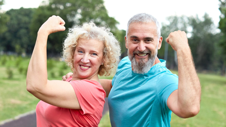 Senior white man and woman stand together, flexing their arms