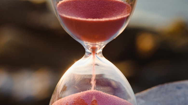 Red sand slips through an hourglass against a blurry background