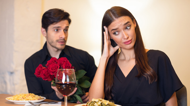 A couple sitting in restaurant, wine and pasta, man pleads while woman covers her face