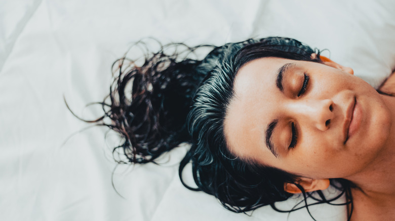 A woman laying down in a bed with wet hair.