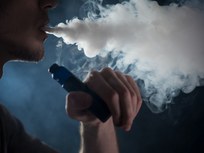Close up of a male vaper exhaling a cloud of steam on a dark background