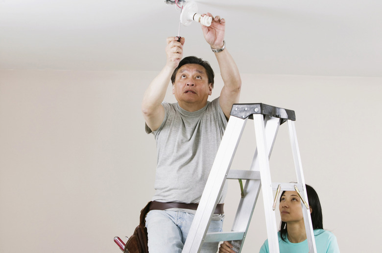 Low angle view of a mid adult man fixing a light fixture with a young woman holding a ladder